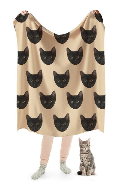 A person holding up a beige blanket with a repeating pattern of a cat's head.