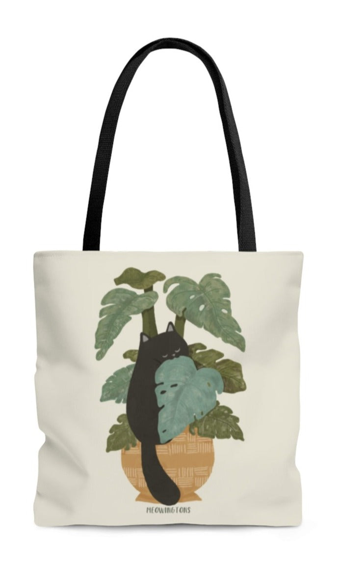 A soft beige cat tote bag with black handles featuring a black cat munching on monstera plant leaves.