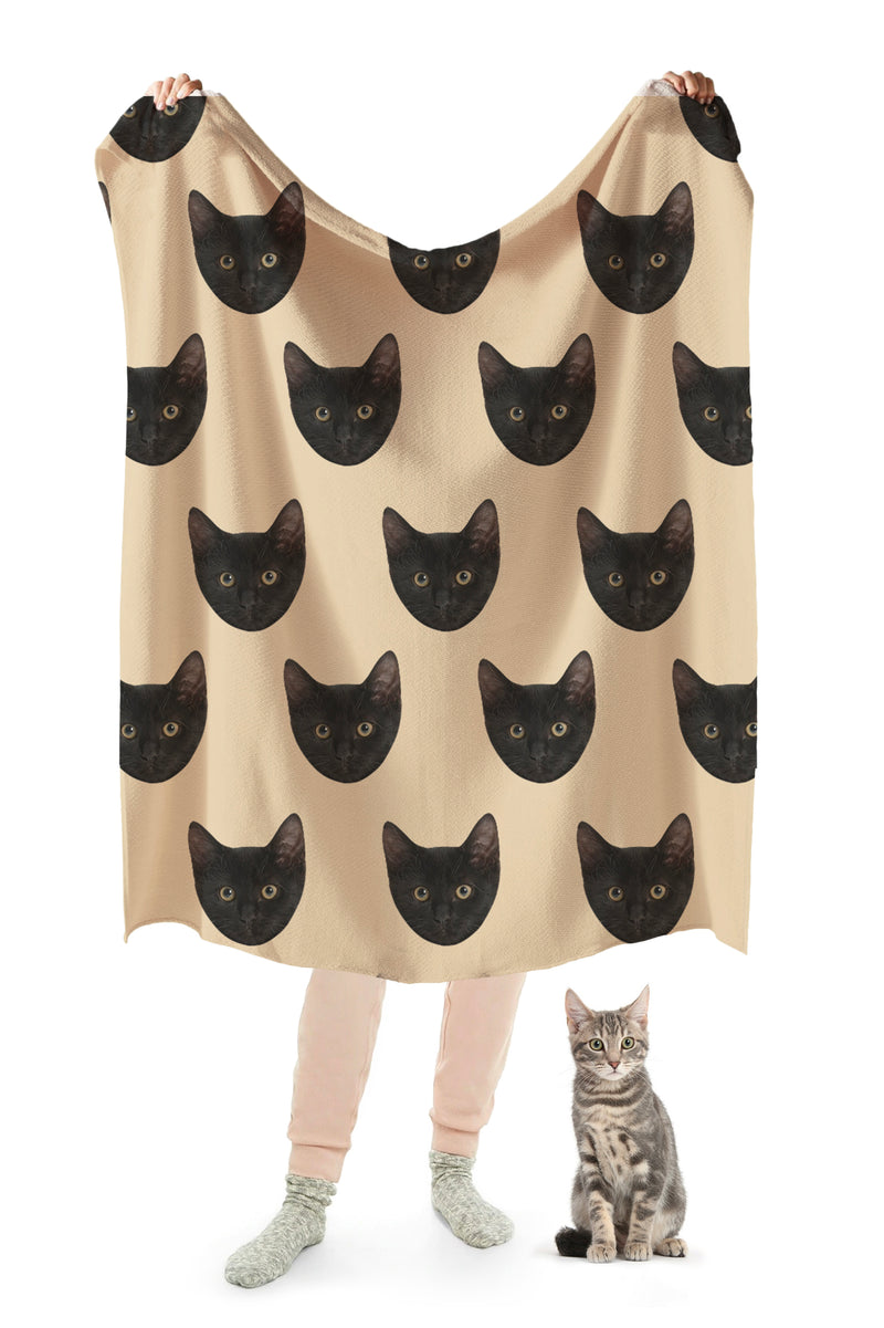 A person holding up a beige blanket with a repeating pattern of a cat&