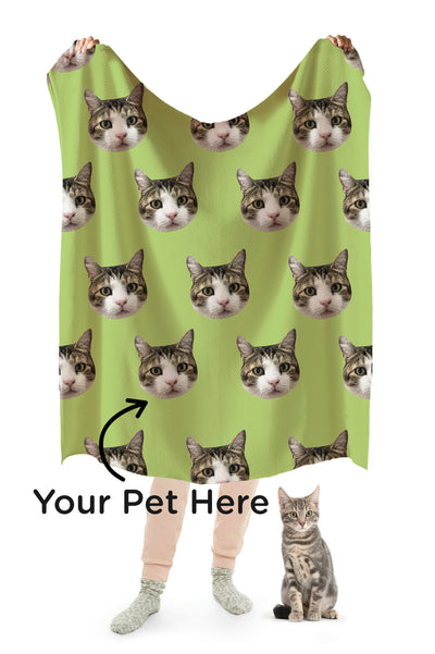 A person holding up a green blanket with a repeating pattern of a cat's head. Text reads "Your Pet Here" with arrow pointing to the cat's faces.