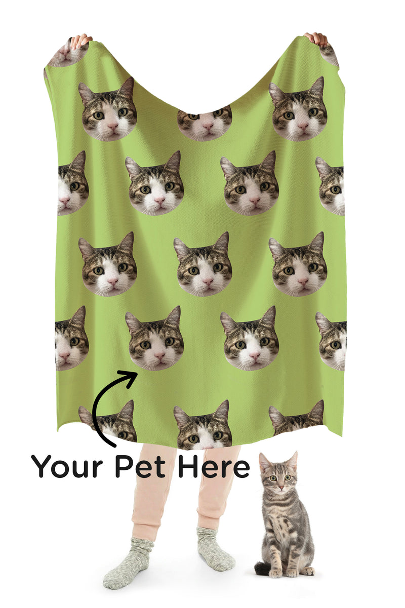 A person holding up a green blanket with a repeating pattern of a cat&